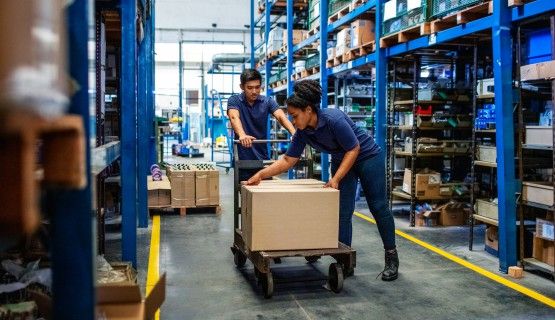 A man and a woman work together to push a trolley through a warehouse