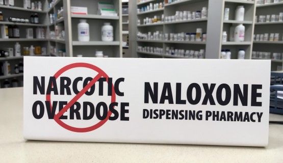 A sign for naloxone on a pharmacy counter