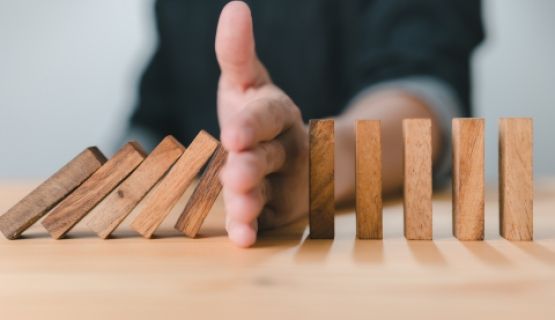 A line of blocks tipping over, a hand stops them from falling.
