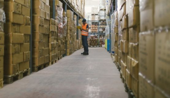 A warehouse worker looks at a tablet among stacks of boxes