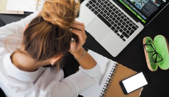 An overhead shot of a woman holding her head in front of a laptop