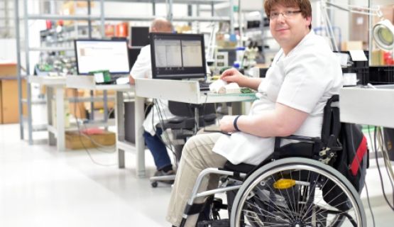 A computer technician who uses a wheelchair works at his station