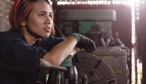 female factory worker sitting on floor with tools, looking worried about what to do