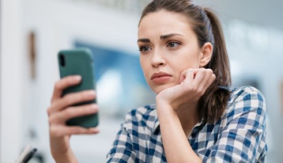 A young woman looks at her phone in frustration and exasperation