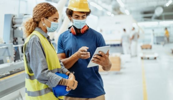 Two workers wearing masks look at a tablet together