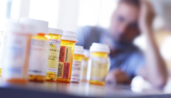 A man with his head in his hand looks at a row of empty pill bottles