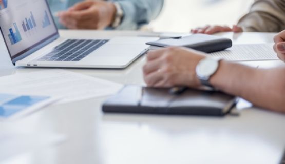 Closeup of hands around documents and a laptop in a business meeting