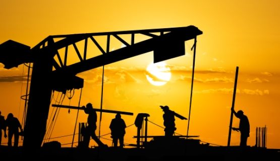 Silhouettes of construction workers against an orange sky