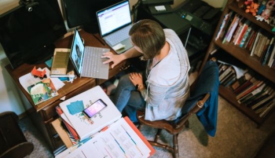 An overhead shot of a teacher, sitting in front of two laptops in a cramped corner of her home office