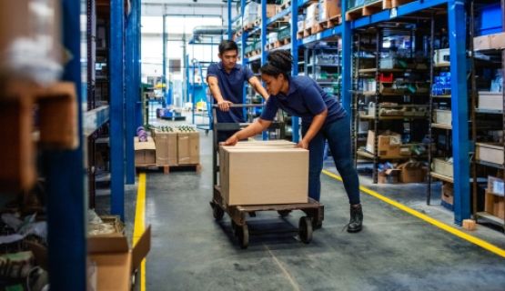 A man and a woman work together to push a trolley through a warehouse
