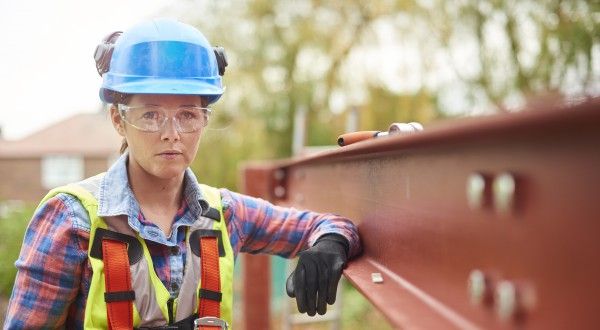 A female construction worker stands next to a steel girder